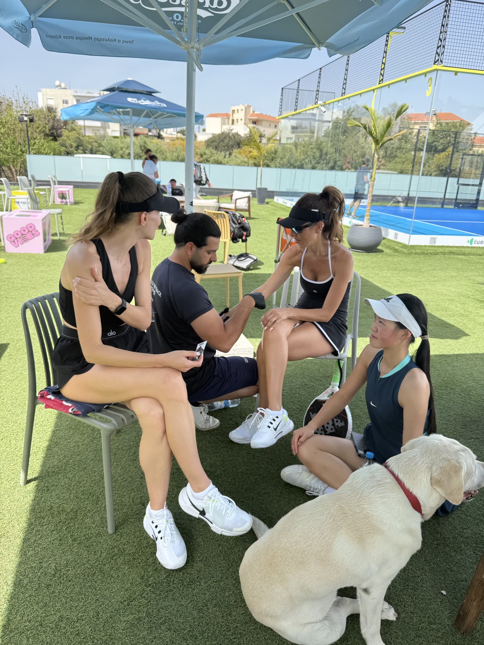 Padel Camp Cyprus group relaxing courtside with a dog after training
